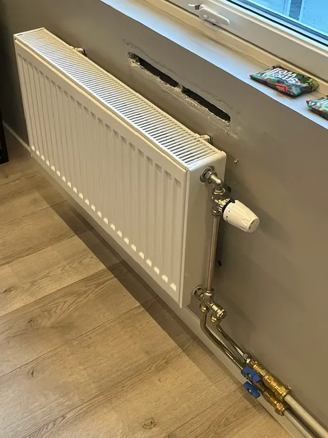 Radiator under vindu med synlige rør og termostatventil