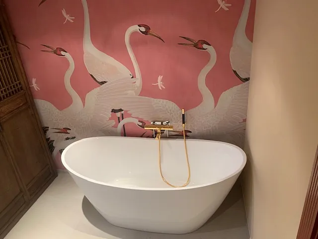 Frittstående badekar med gullfarget armatur og rosa tapet med fuglemotiv